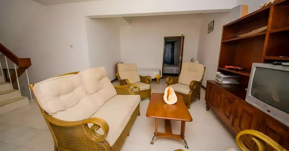 Apartment living room with cane sofa and armchairs, a television and a timber shelf unit