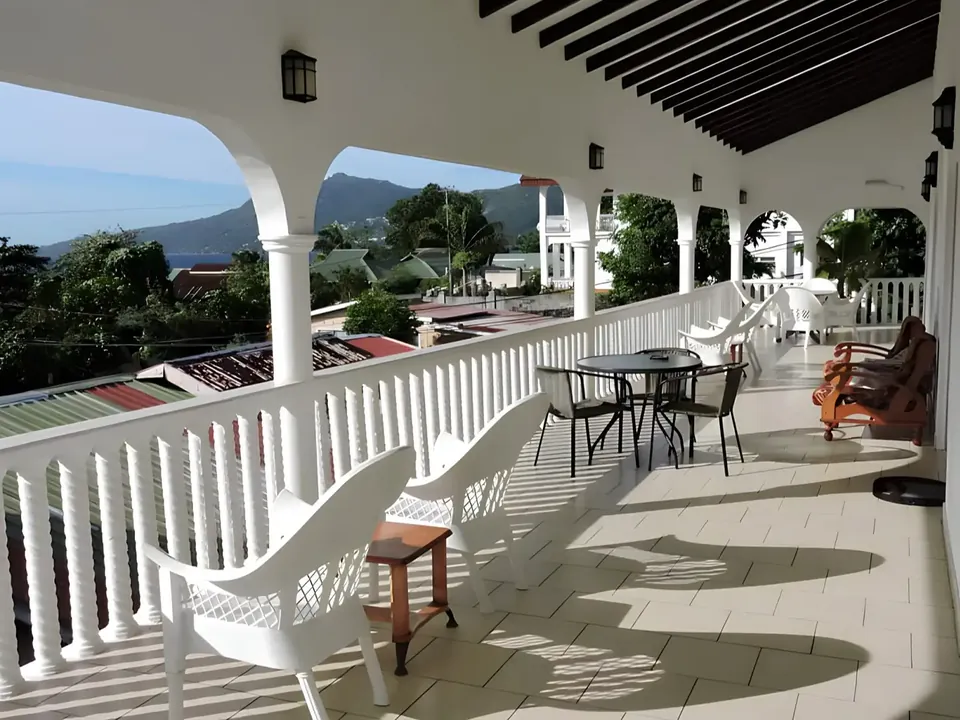 Arched veranda with white railings, looking over rooftops to the sea and the hills